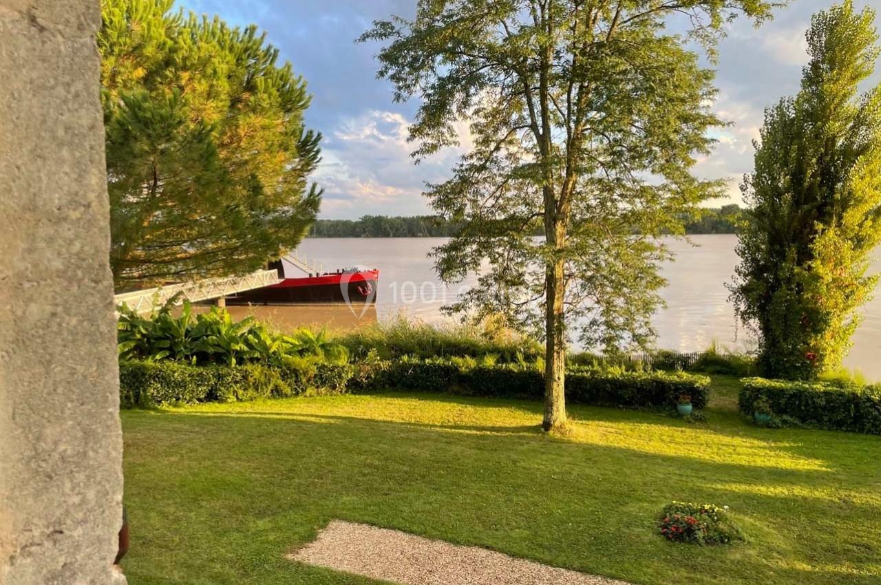 Bateau rouge amarré sur une rivière bordée de végétation, avec pelouse et arbres au premier plan.