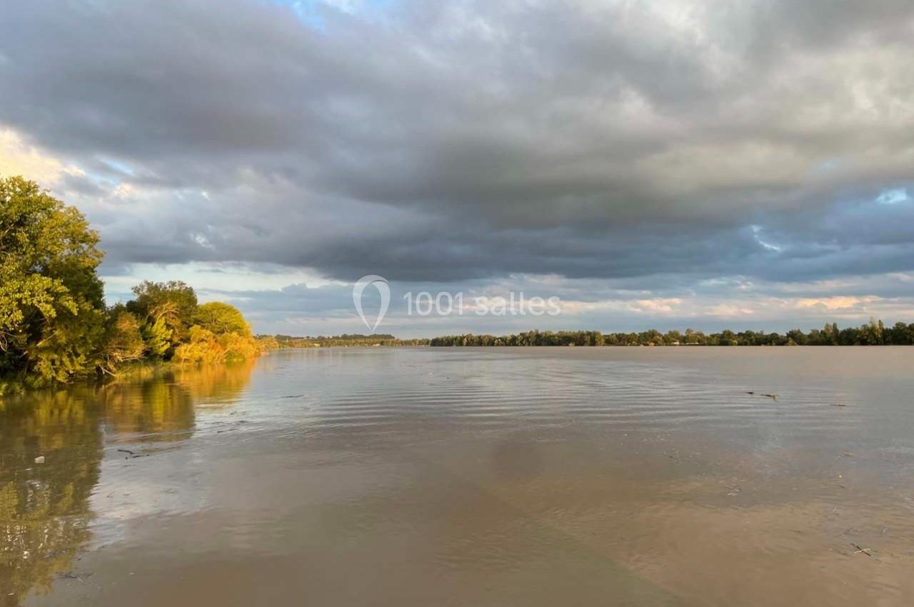 Rivière calme au coucher du soleil, bordée d'arbres et surplombée par un ciel partiellement nuageux.