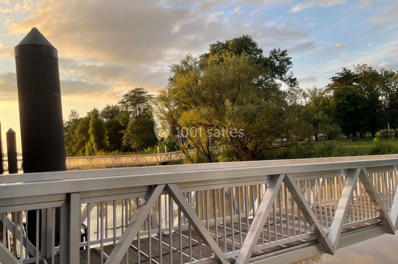 Passerelle en métal surplombant une rivière calme, entourée d'arbres et éclairée par une lumière douce au coucher du soleil.