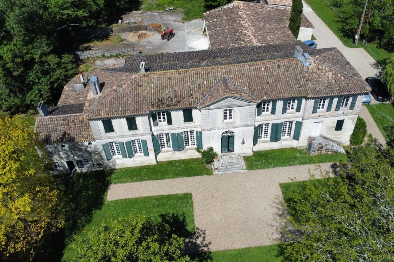 Vue aérienne d'une grande bâtisse ancienne en pierre avec toit en tuiles, entourée de verdure et d'allées gravillonnées.