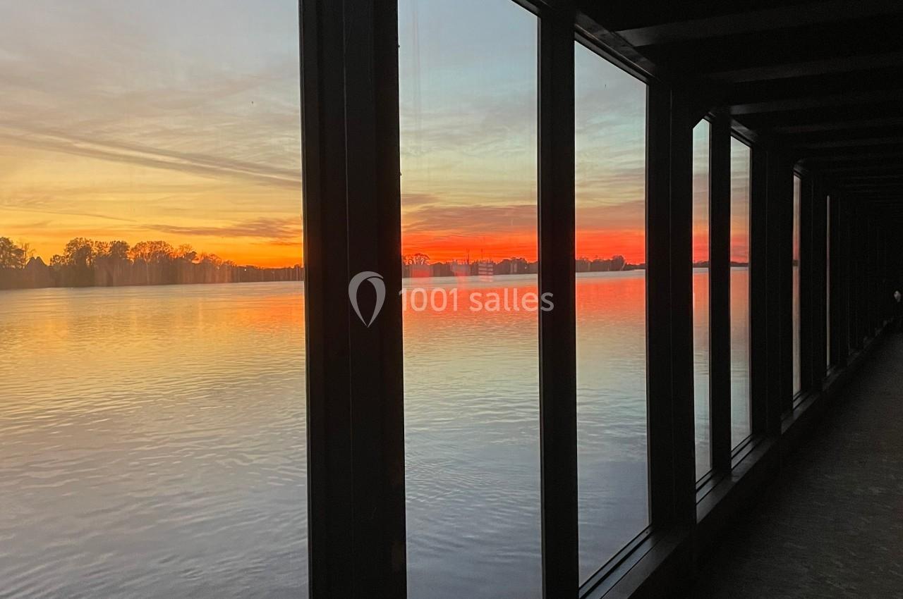 Vue d'un coucher de soleil vibrant à travers de grandes fenêtres donnant sur une étendue d'eau calme.