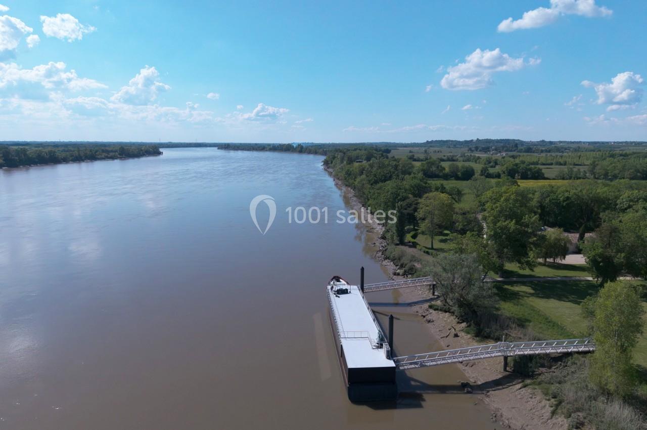 Vue aérienne d'une rivière bordée de végétation avec un ponton et une passerelle sur la rive droite.
