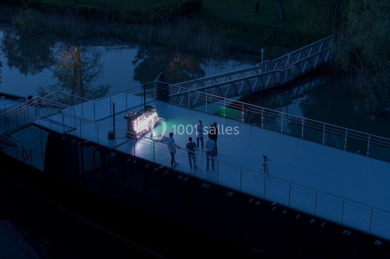 Un groupe de personnes se tient près d'une table lumineuse sur le pont d'un bateau, de nuit, près d'un quai.