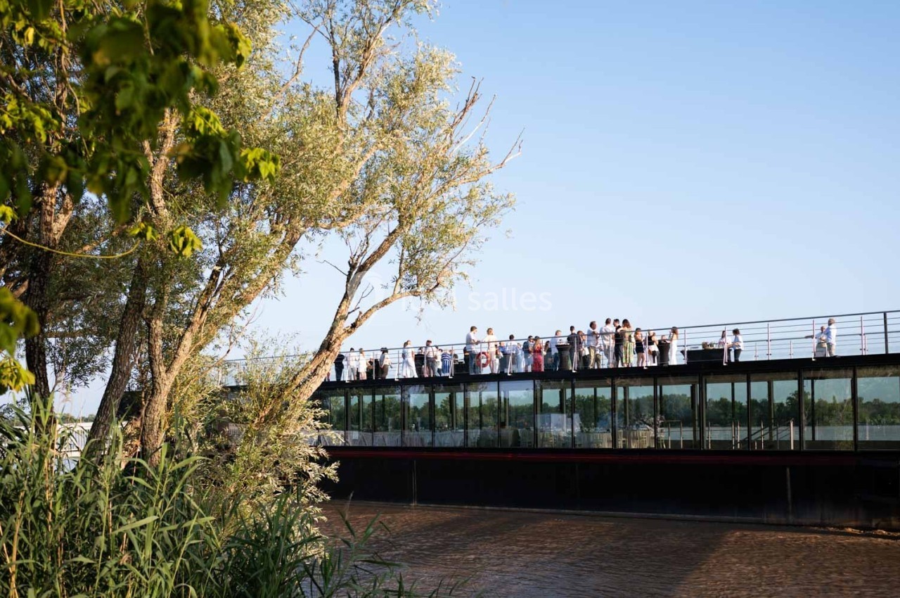 Groupe de personnes rassemblées sur une passerelle en verre au-dessus d'un cours d'eau, entourée de végétation.