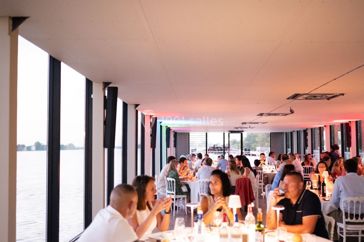 Des personnes dînent dans une salle lumineuse avec de grandes baies vitrées donnant sur un plan d'eau.
