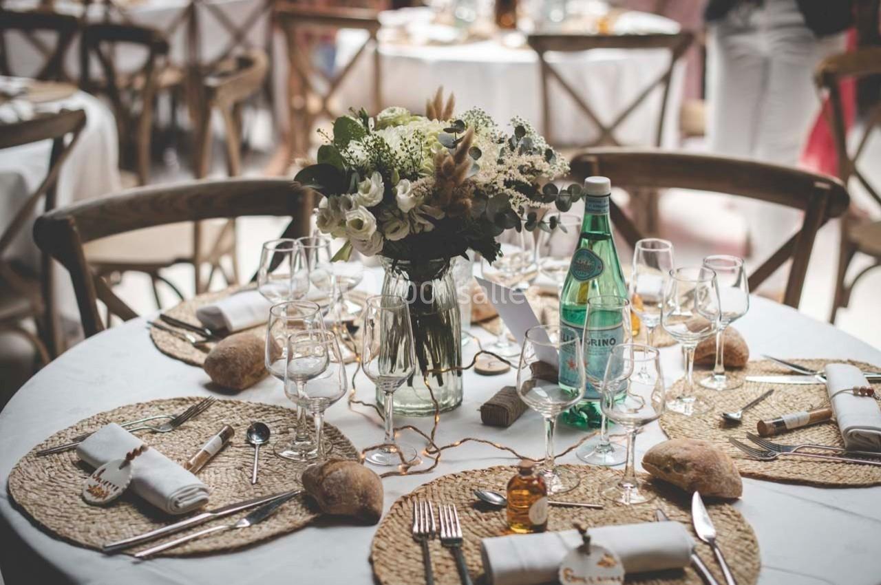 Table dressée avec des assiettes, couverts, serviettes, pain, un bouquet de fleurs et une bouteille d'eau minérale.