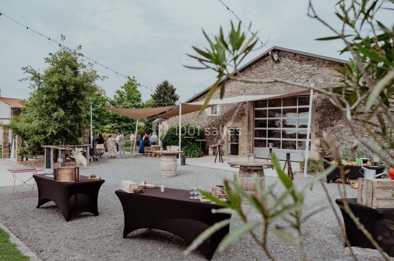 Cour extérieure avec tables et tonneaux, devant un bâtiment en pierre, utilisée pour un événement en plein air.