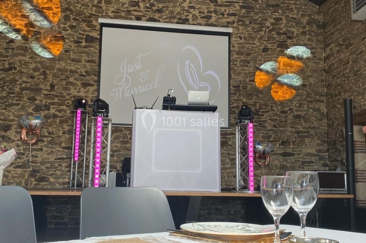 Salle de réception décorée avec une table dressée au premier plan et un espace DJ équipé en arrière-plan.