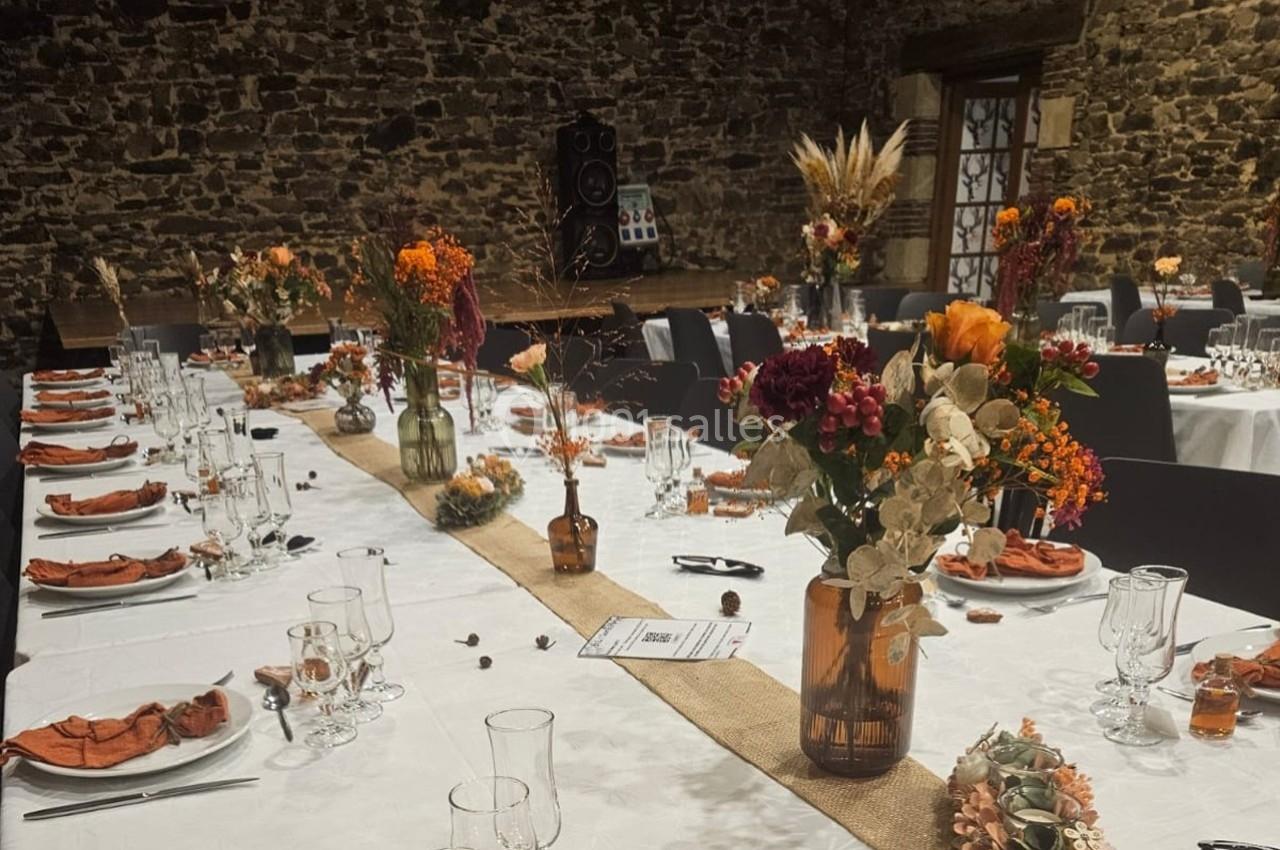 Tables décorées pour un événement, ornées de fleurs séchées et vases en verre, dans une salle en pierre avec ambiance…