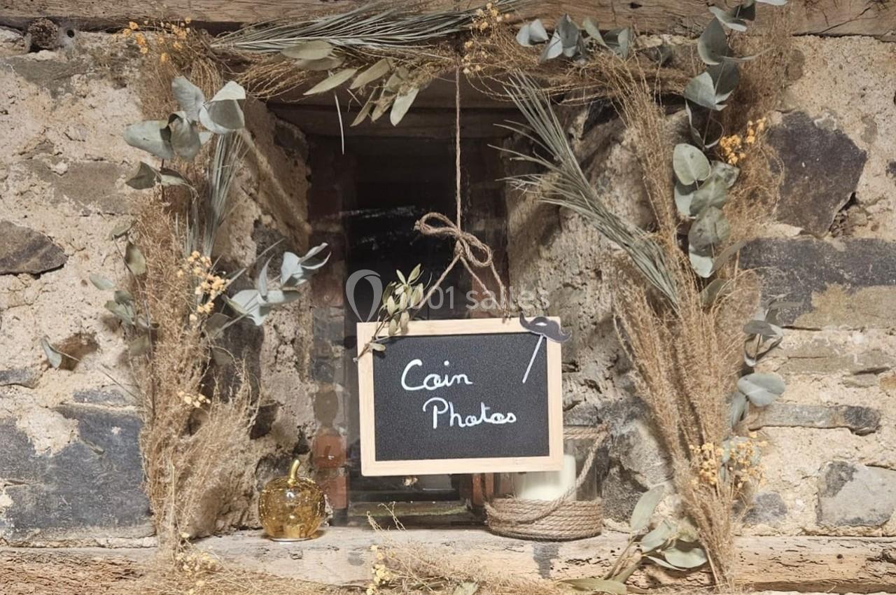 Ardoise suspendue avec l'inscription ’Coin Photos’, entourée de décorations végétales sur un mur en pierre.