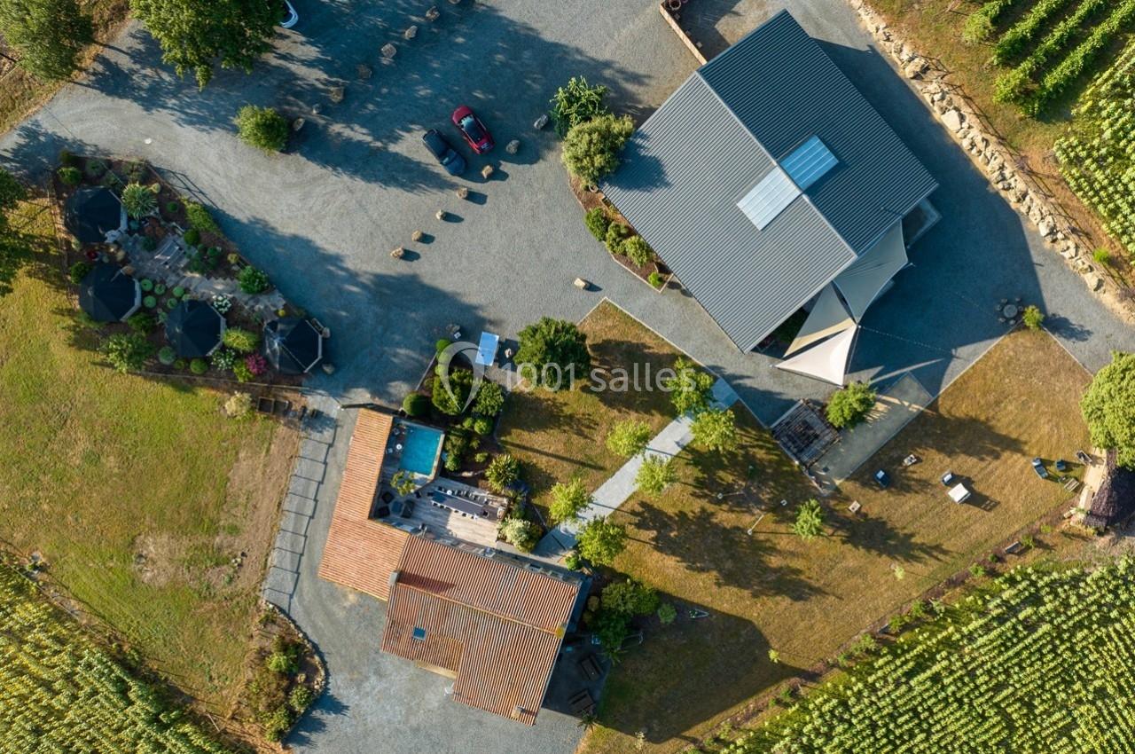 Vue aérienne d'un domaine avec bâtiments, piscine, terrasse et vignobles environnants sous un ciel dégagé.