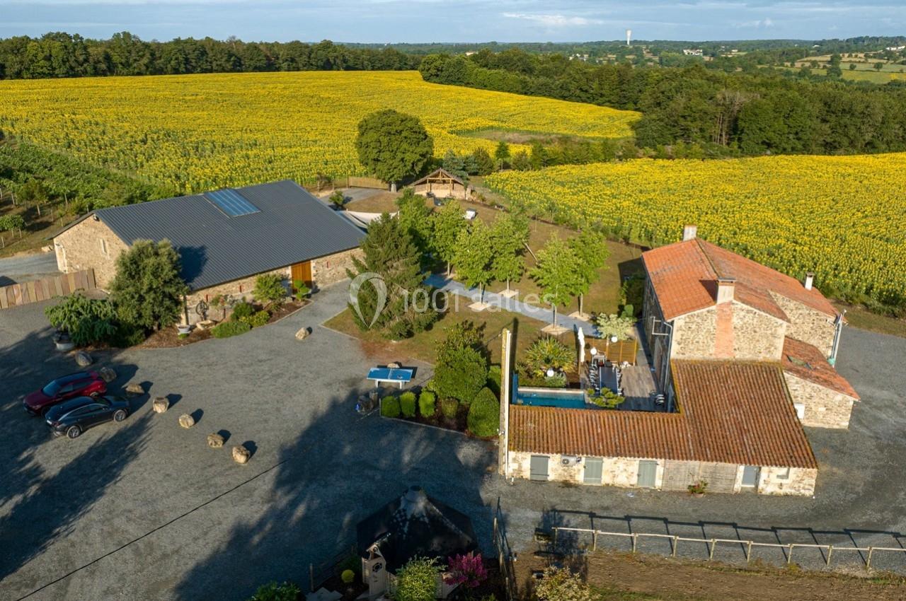 Vue aérienne d'un domaine rural avec bâtiments en pierre, piscine, arbres et champs de tournesols environnants.