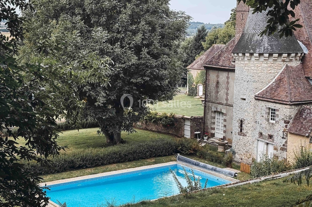 Vue d'une maison en pierre avec une piscine entourée de verdure dans un cadre rural.
