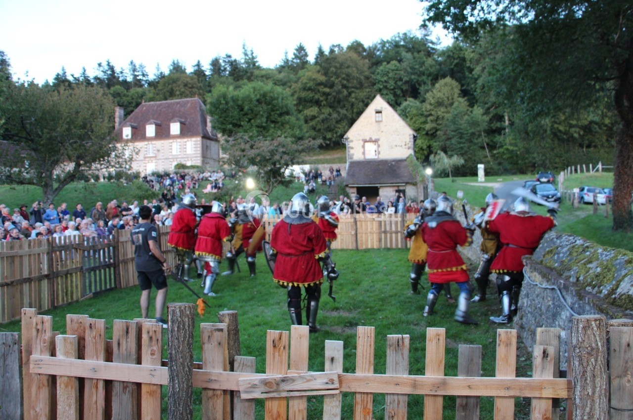 Des personnes en armures médiévales participent à une reconstitution historique dans un espace extérieur clôturé.