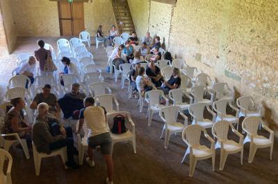 Salon rustique avec murs en pierre, canapés en cuir, table basse et porte ouverte donnant sur un jardin ensoleillé.