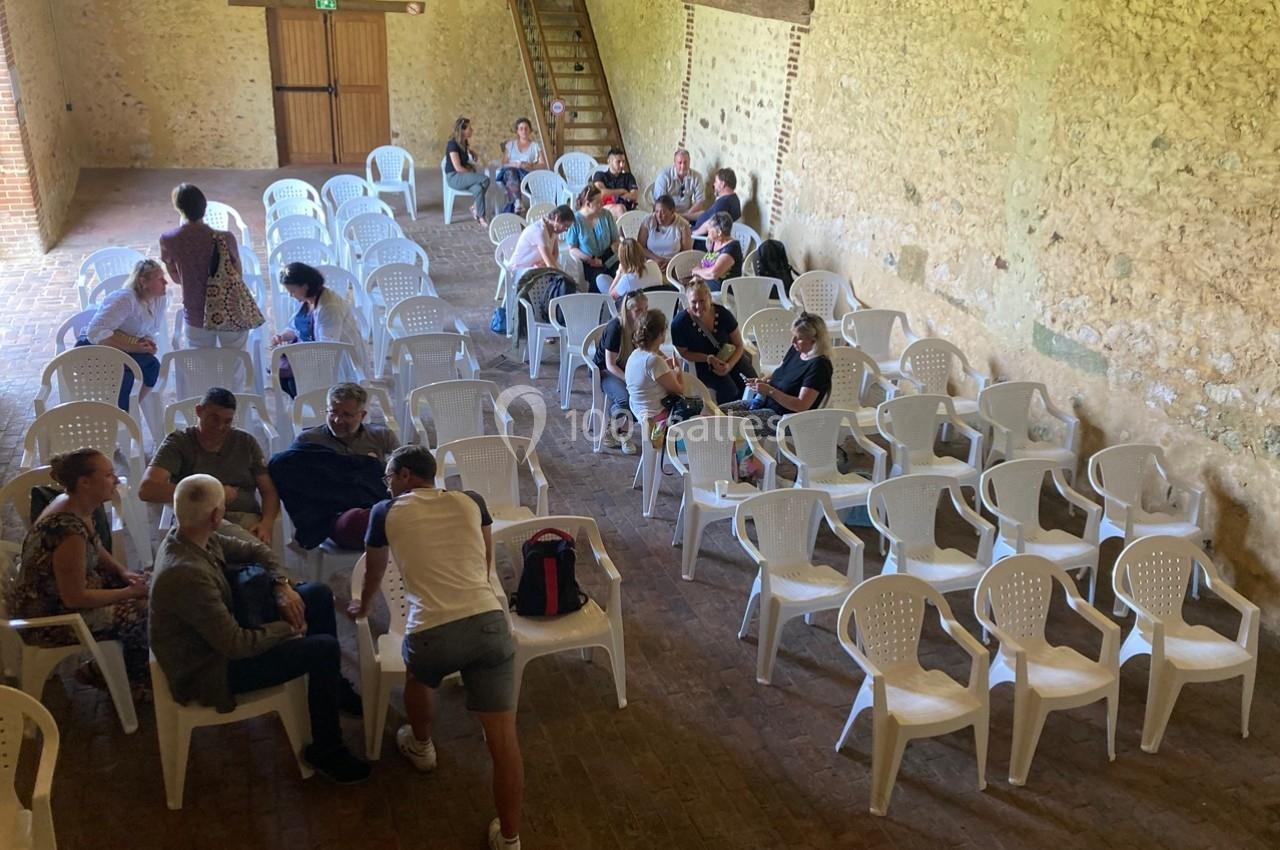 Des personnes assises et discutant dans une salle avec des murs en pierre et des chaises en plastique blanc.