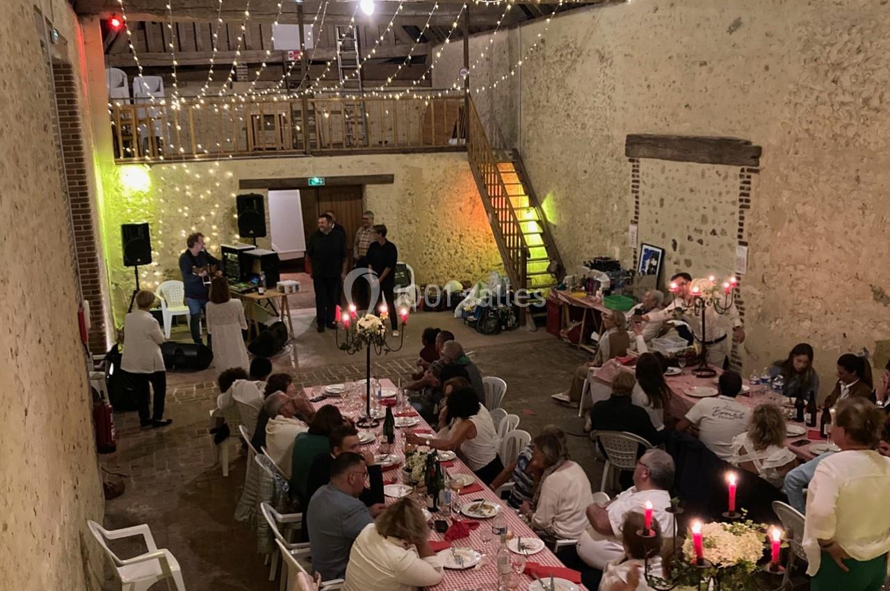 Salle rustique décorée de guirlandes lumineuses, avec des invités attablés et une ambiance conviviale.