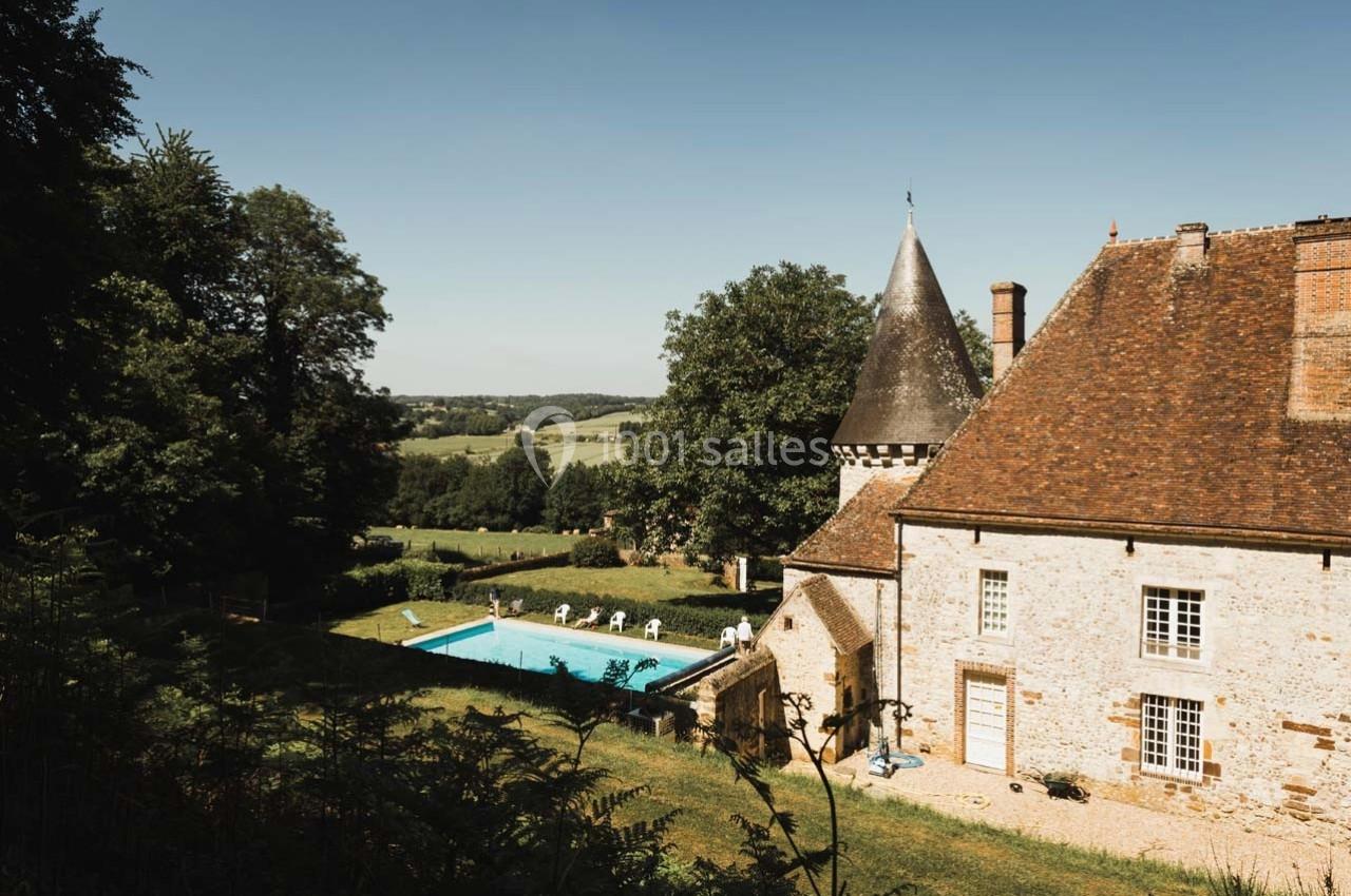 Manoir en pierre avec toit en tuiles, piscine extérieure et paysage rural verdoyant en arrière-plan.