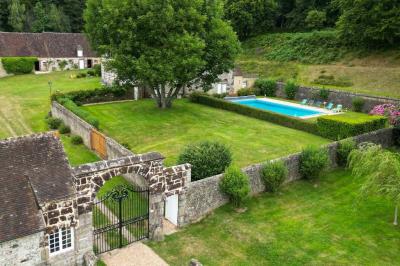 Salon rustique avec murs en pierre, canapés en cuir, table basse et porte ouverte donnant sur un jardin ensoleillé.