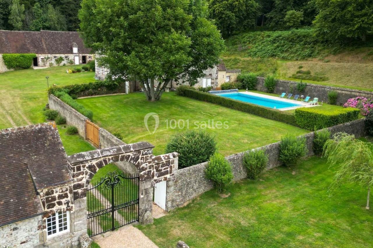 Vue aérienne d'une propriété avec jardin, piscine, bâtiments en pierre et espaces verts entourés de haies.