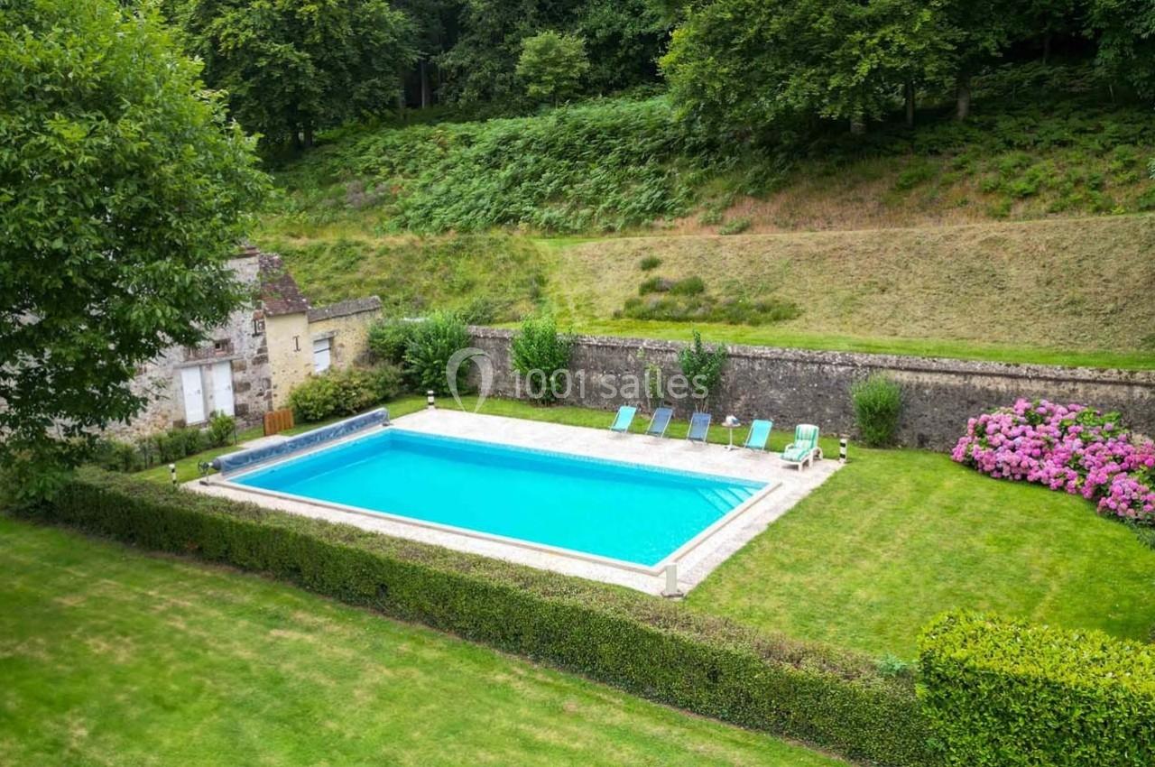 Piscine rectangulaire entourée de pelouse, de chaises longues et de végétation dans un jardin clos.
