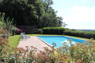 Salon rustique avec murs en pierre, canapés en cuir, table basse et porte ouverte donnant sur un jardin ensoleillé.