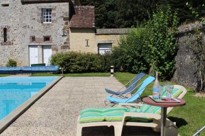 Salon rustique avec murs en pierre, canapés en cuir, table basse et porte ouverte donnant sur un jardin ensoleillé.