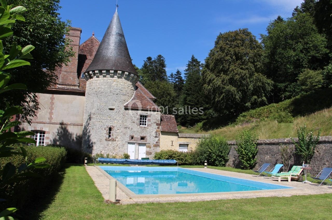 Château en pierre avec une tour, piscine extérieure entourée de chaises longues et jardin verdoyant.