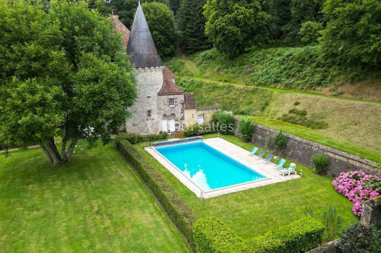 Vue aérienne d'un jardin avec une piscine entourée de chaises longues, près d'une maison en pierre et d'arbres.