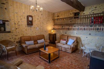 Salon rustique avec murs en pierre, canapés en cuir, table basse et porte ouverte donnant sur un jardin ensoleillé.