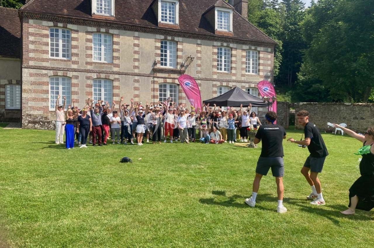 Groupe de personnes rassemblées devant un bâtiment en briques et pierre, sur une pelouse, avec des drapeaux roses.