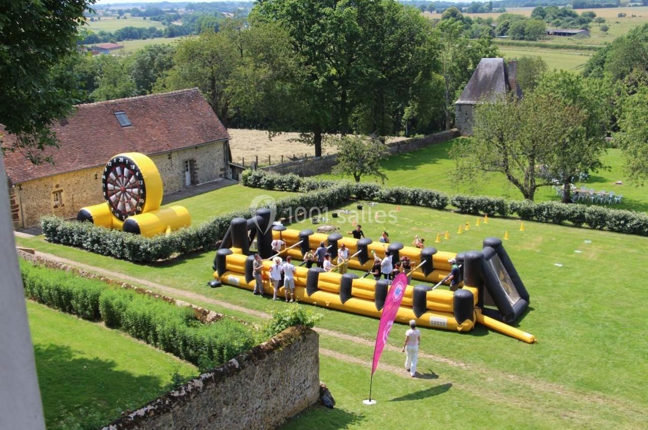 Structure gonflable jaune et noire avec des participants, installée dans un jardin entouré de bâtiments anciens.