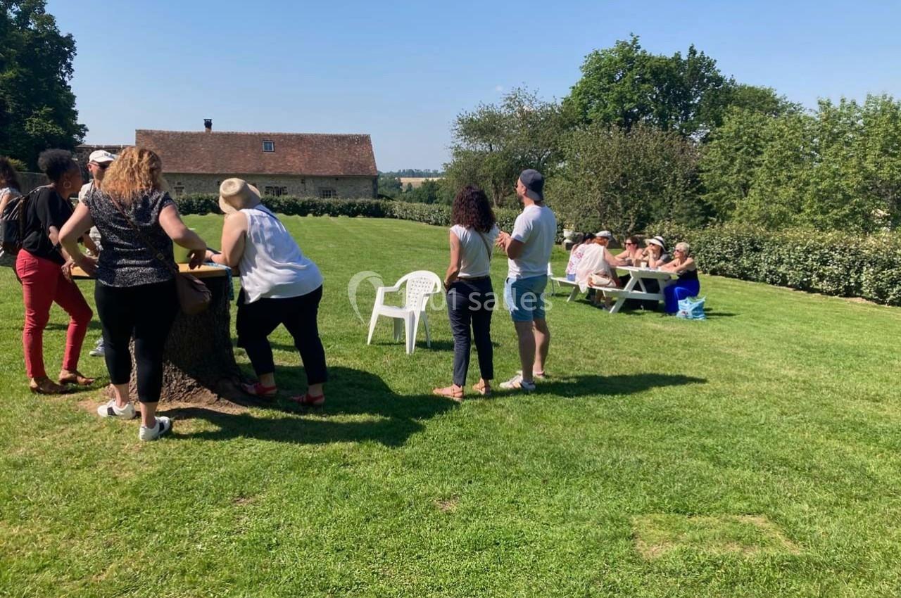 Personnes réunies dans un jardin, discutant debout près d'une table ou assises à une autre table en arrière-plan.
