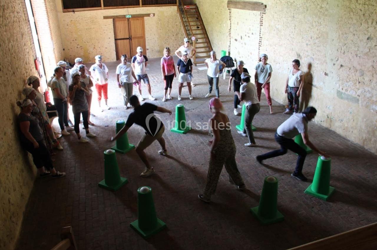 Des personnes participent à une activité ludique en intérieur, disposées autour de cônes verts dans une salle en pierre.