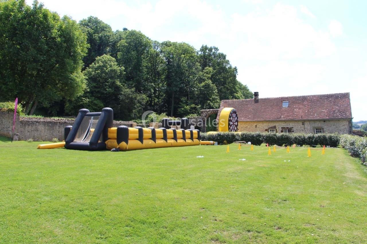 Structure gonflable jaune et noire installée sur une pelouse, avec une maison en pierre et des arbres en arrière-plan.