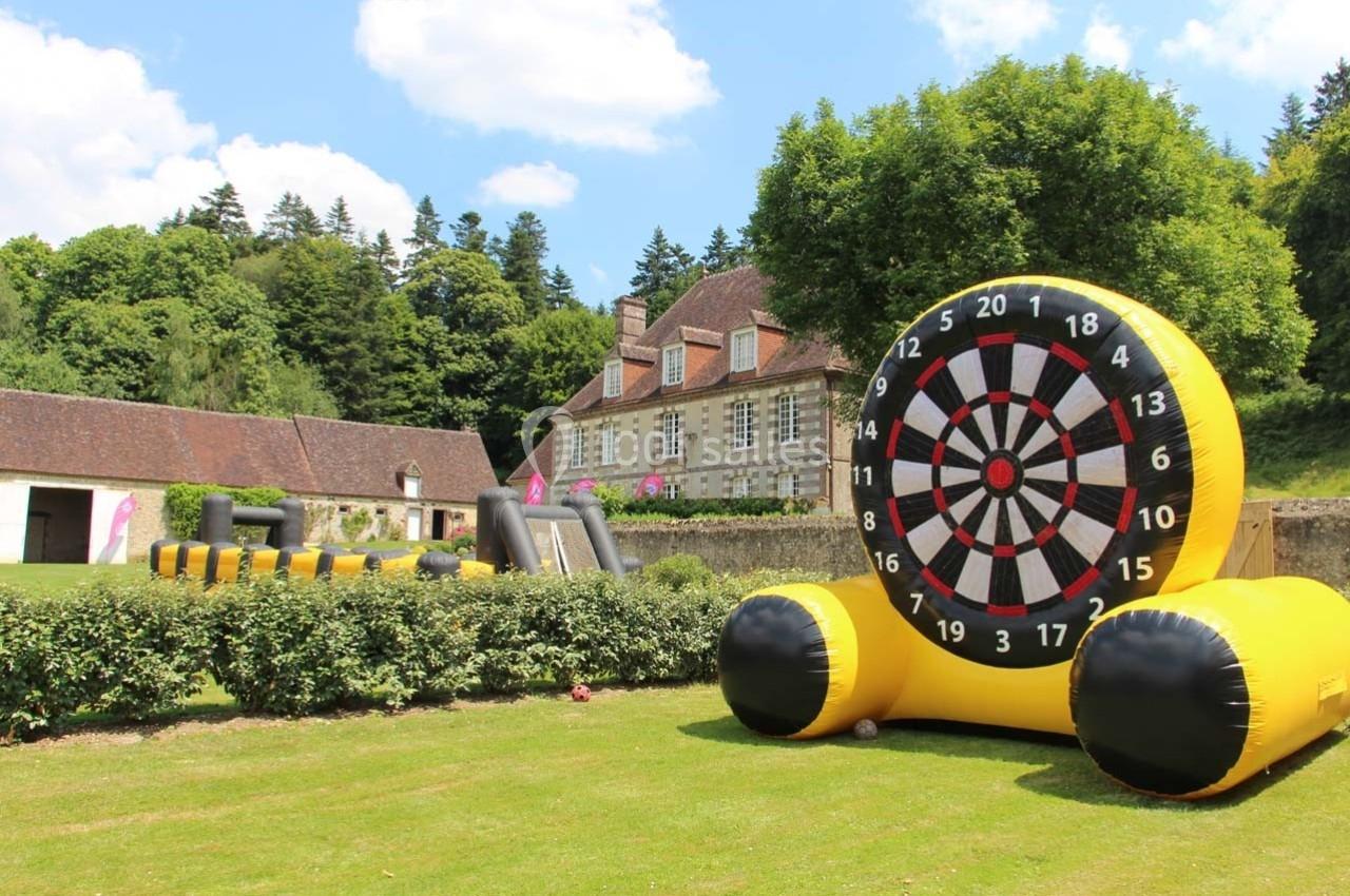 Cible géante gonflable installée sur une pelouse devant un bâtiment ancien entouré de verdure.