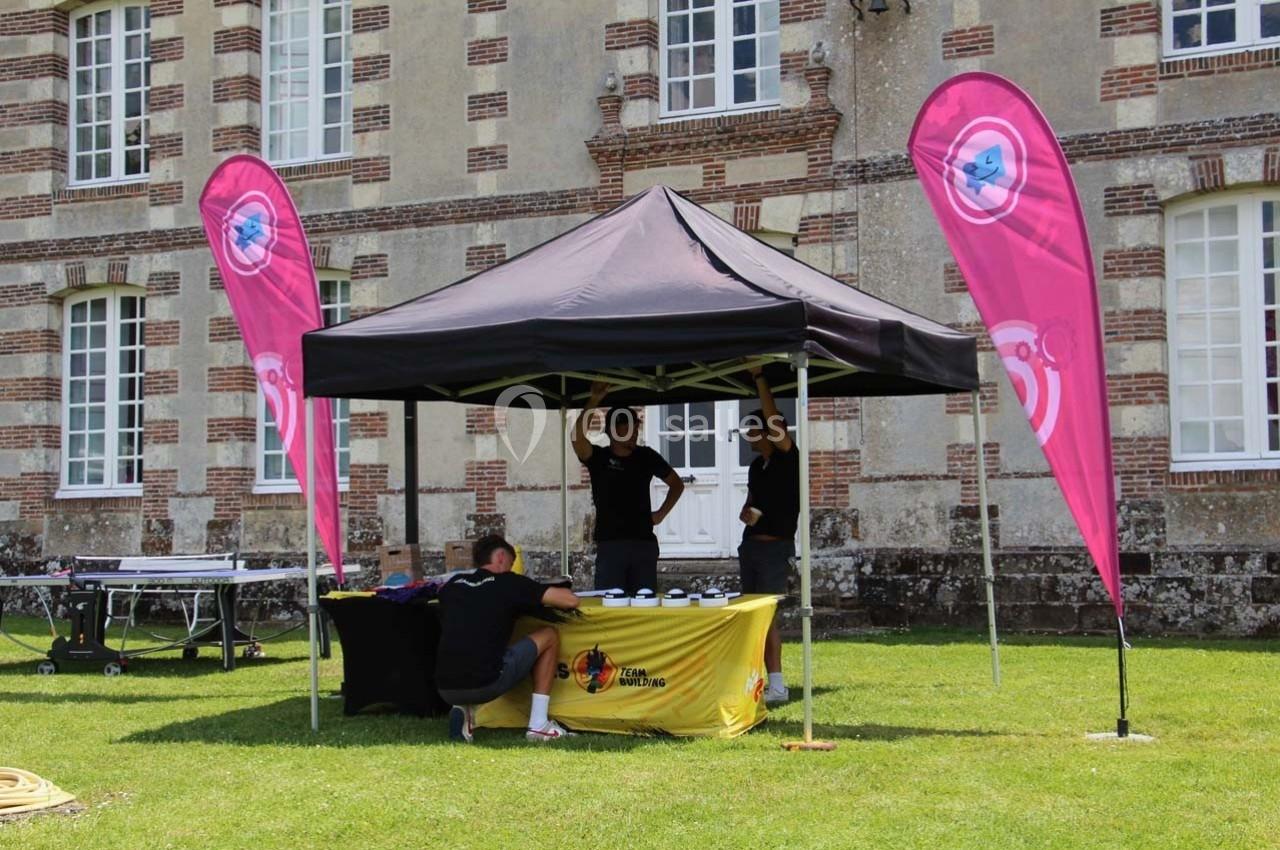 Stand sous une tente noire avec trois personnes, des drapeaux roses et un bâtiment en arrière-plan.