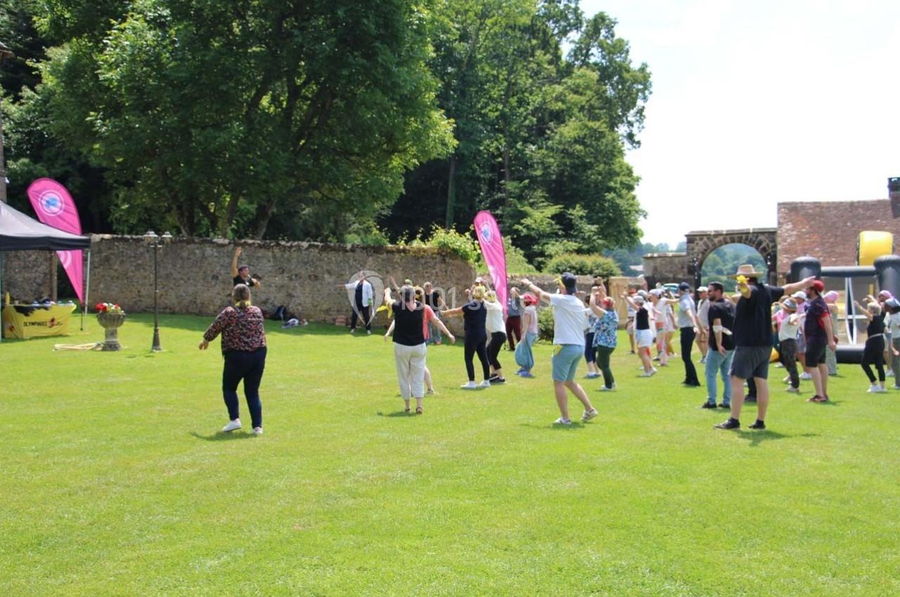Groupe de personnes participant à une activité en plein air sur une pelouse, avec des arbres et des structures en arrière…