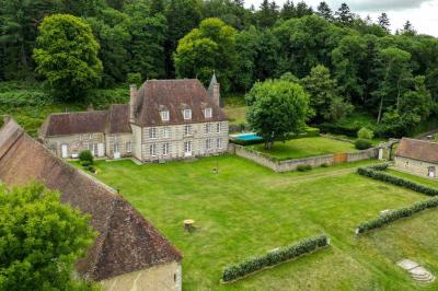 Salon rustique avec murs en pierre, canapés en cuir, table basse et porte ouverte donnant sur un jardin ensoleillé.
