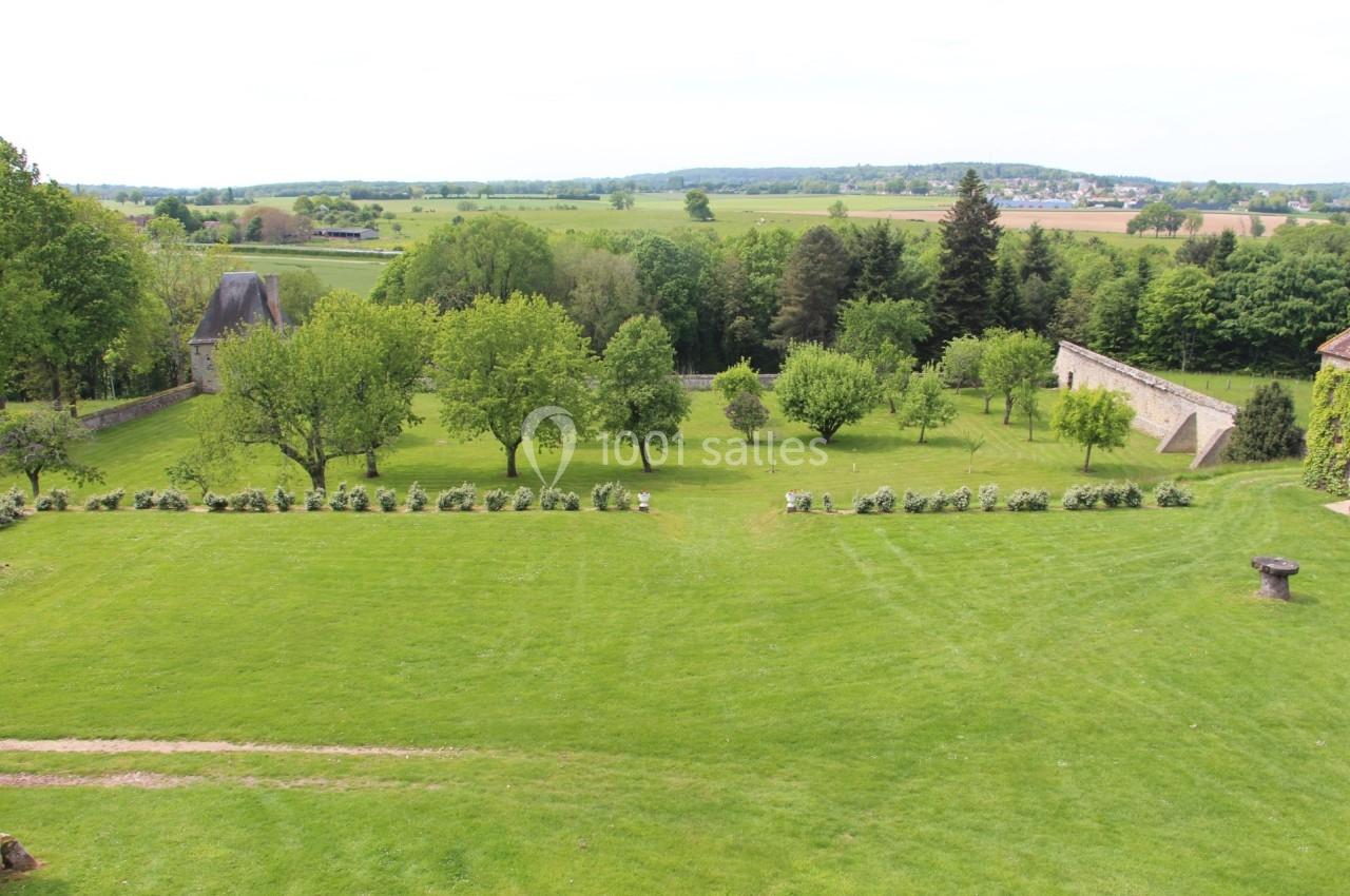 Vue d'un grand jardin verdoyant avec des arbres, des haies et des murs en pierre, entouré d'une campagne vallonnée.