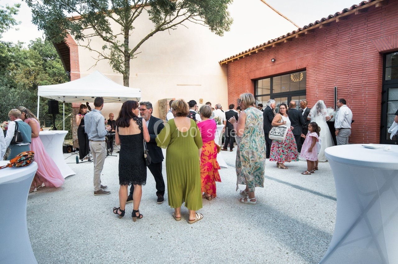 Groupe de personnes rassemblées dans une cour extérieure, près de tables hautes et d'une tente blanche.