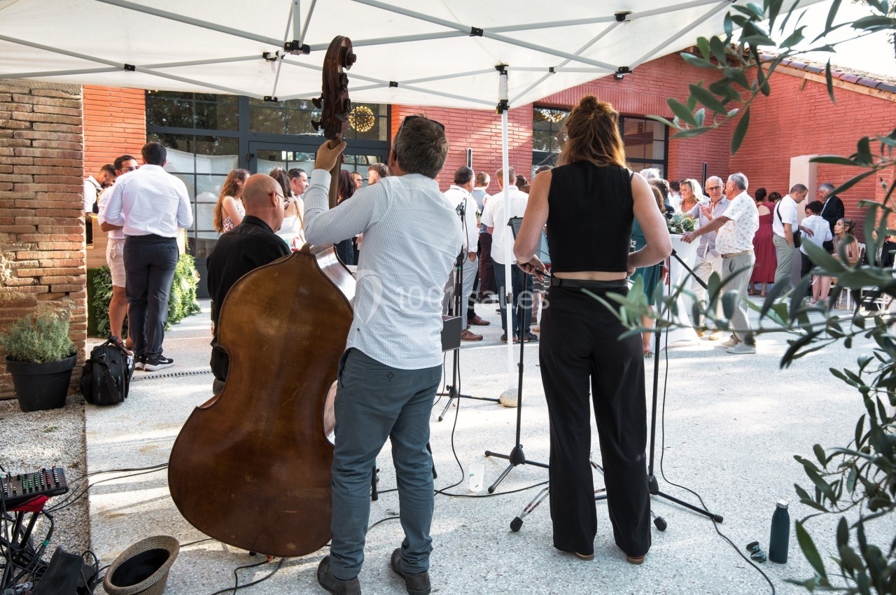 Deux musiciens jouent sous un auvent lors d'un événement en extérieur, avec des invités en arrière-plan.