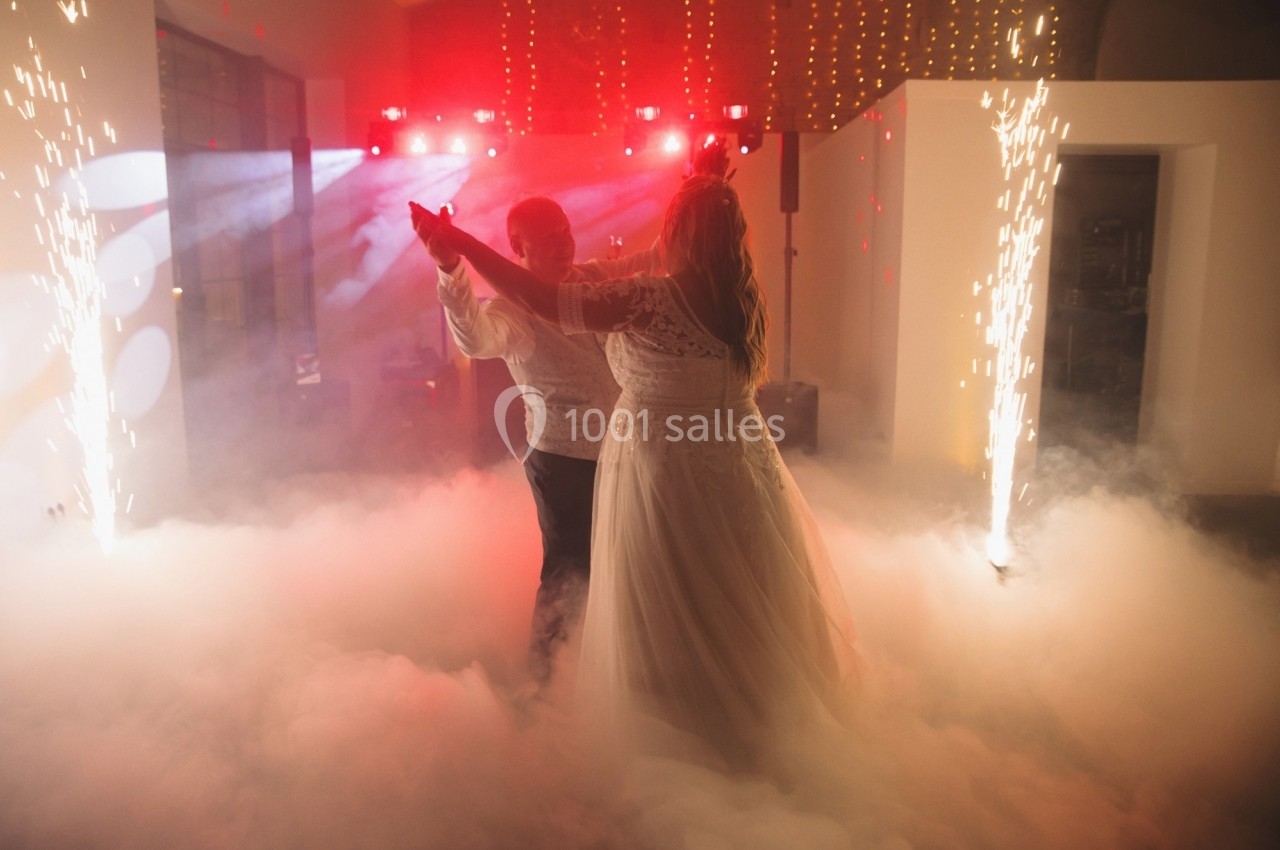 Un couple danse au milieu de la fumée et des étincelles dans une salle illuminée de lumières rouges.