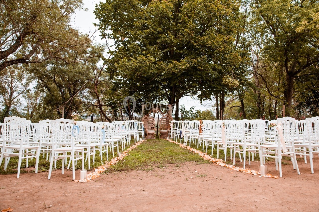 Chaises blanches disposées en rangées dans un jardin, formant une allée centrale menant à une arche décorative.