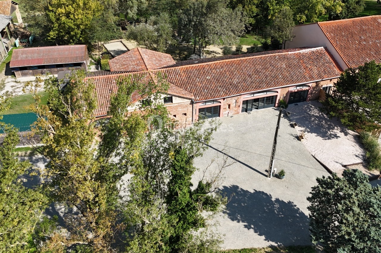 Vue aérienne d'un bâtiment en briques avec toit en tuiles, entouré d'arbres et d'une cour pavée.
