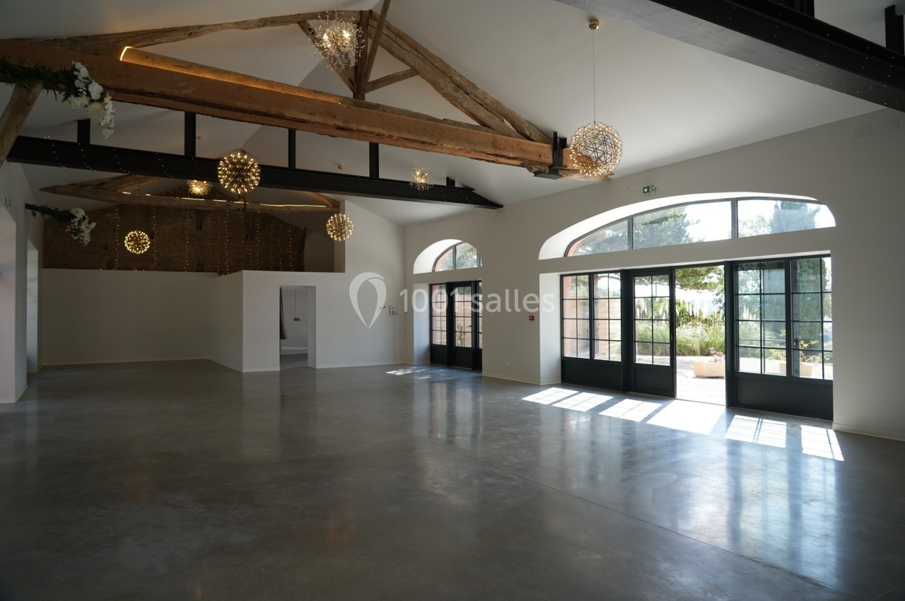 Salle lumineuse avec poutres apparentes, grandes baies vitrées et sol en béton poli, donnant sur un espace extérieur…