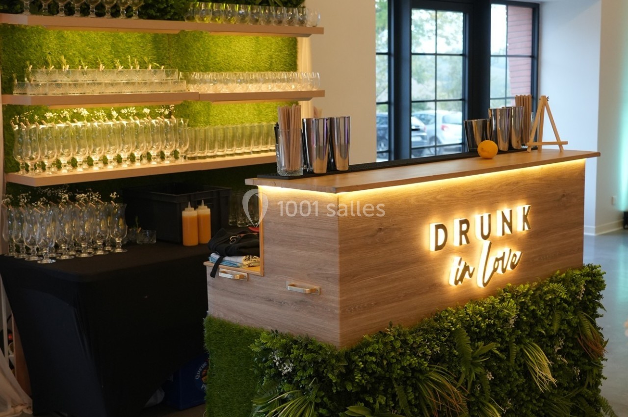 Bar en bois avec éclairage ’Drunk in Love’, décoré de plantes, verres alignés et accessoires de cocktail à disposition.