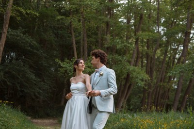 Une mariée en robe blanche tient un bouquet coloré face à un homme en costume clair dans un jardin verdoyant.