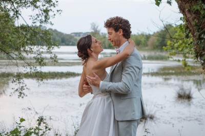 Une mariée en robe blanche tient un bouquet coloré face à un homme en costume clair dans un jardin verdoyant.