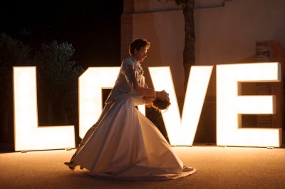 Une mariée en robe blanche tient un bouquet coloré face à un homme en costume clair dans un jardin verdoyant.